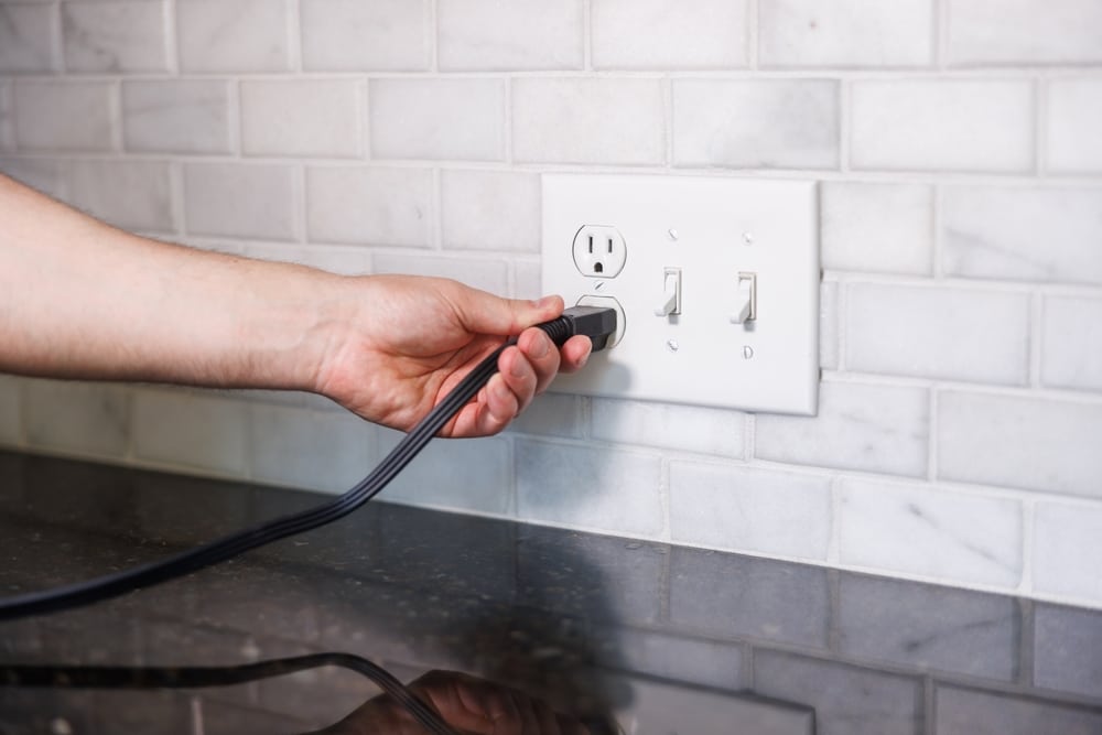 Hand,Turning,Off,Light,Switch,With,Electrical,Outlet,In,Background